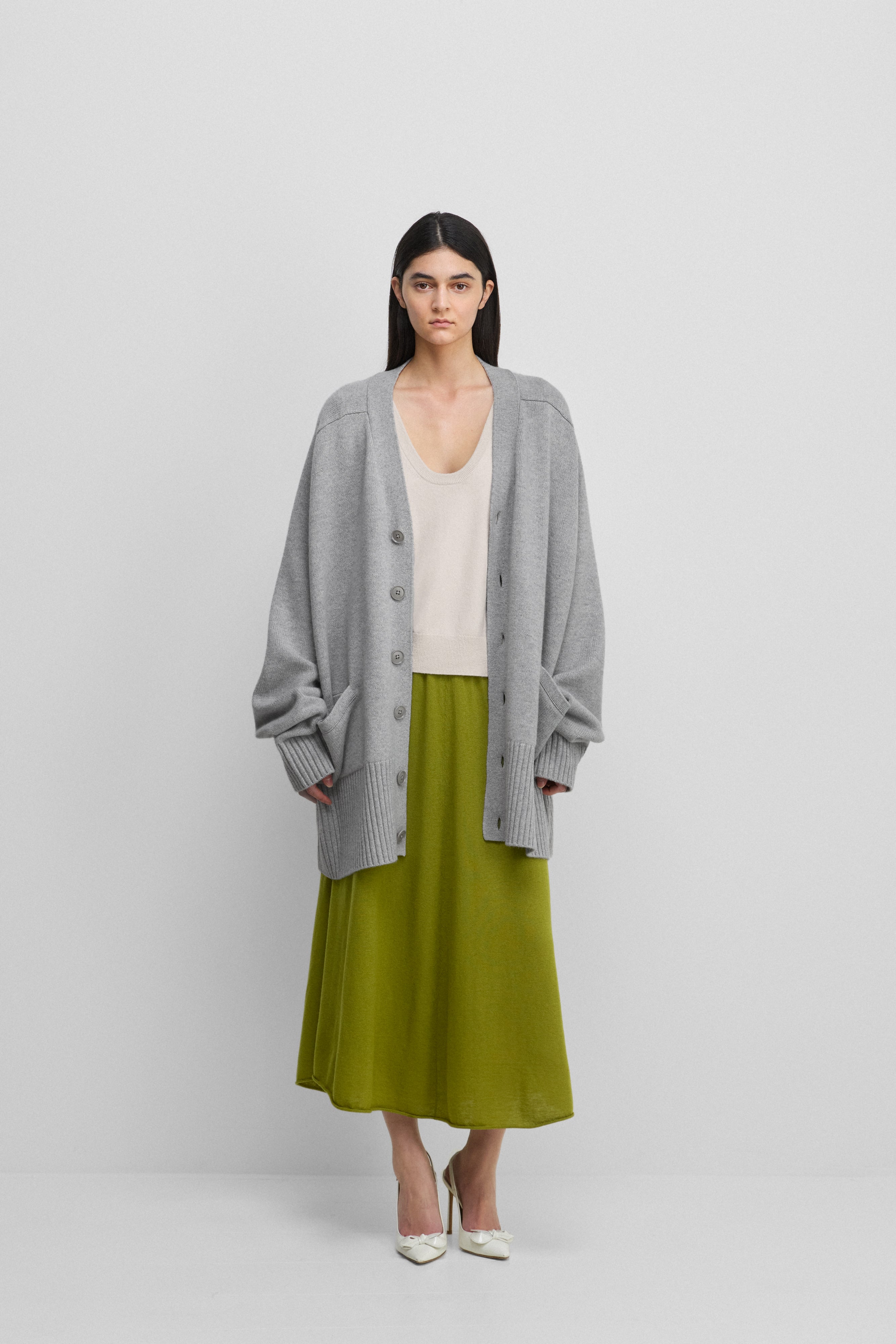 woman wearing a grey oversized chunky cashmere button-up cardigan with pockets, styled with a skirt.