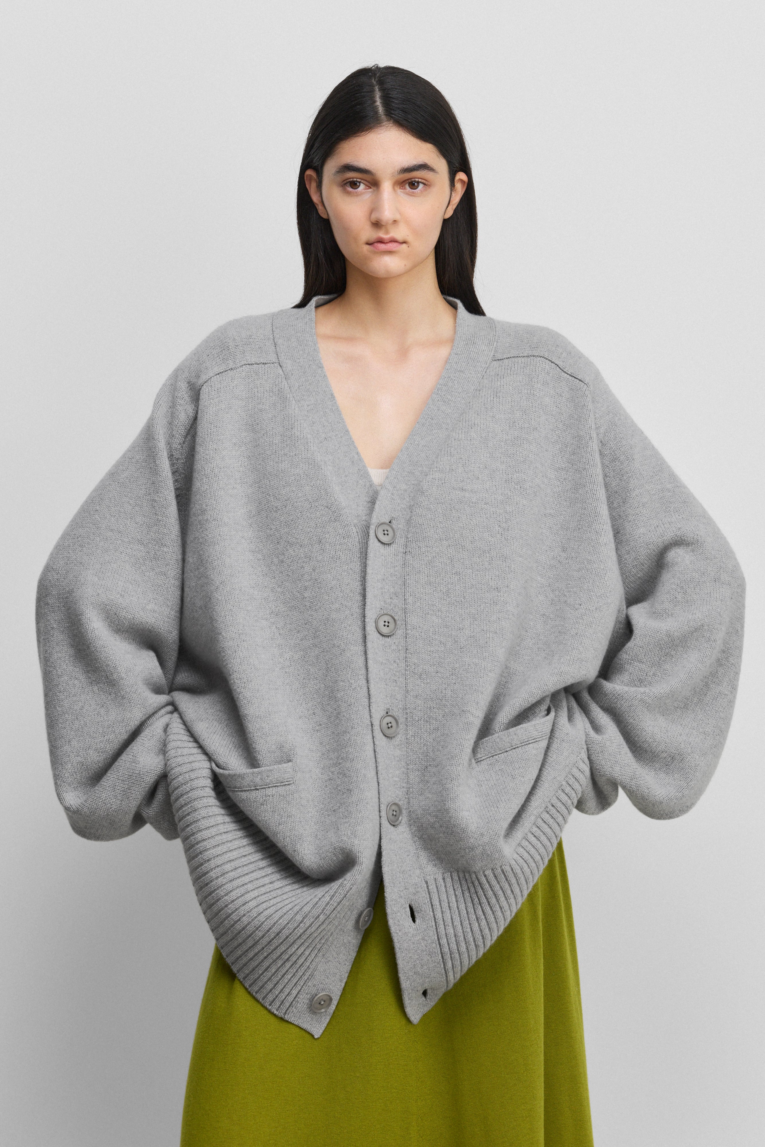 woman wearing a grey oversized chunky cashmere cardigan with six corozo buttons and pockets.