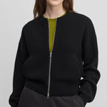 woman wearing a black cashmere crew-neck cardigan with a metallic zipper and side pockets.