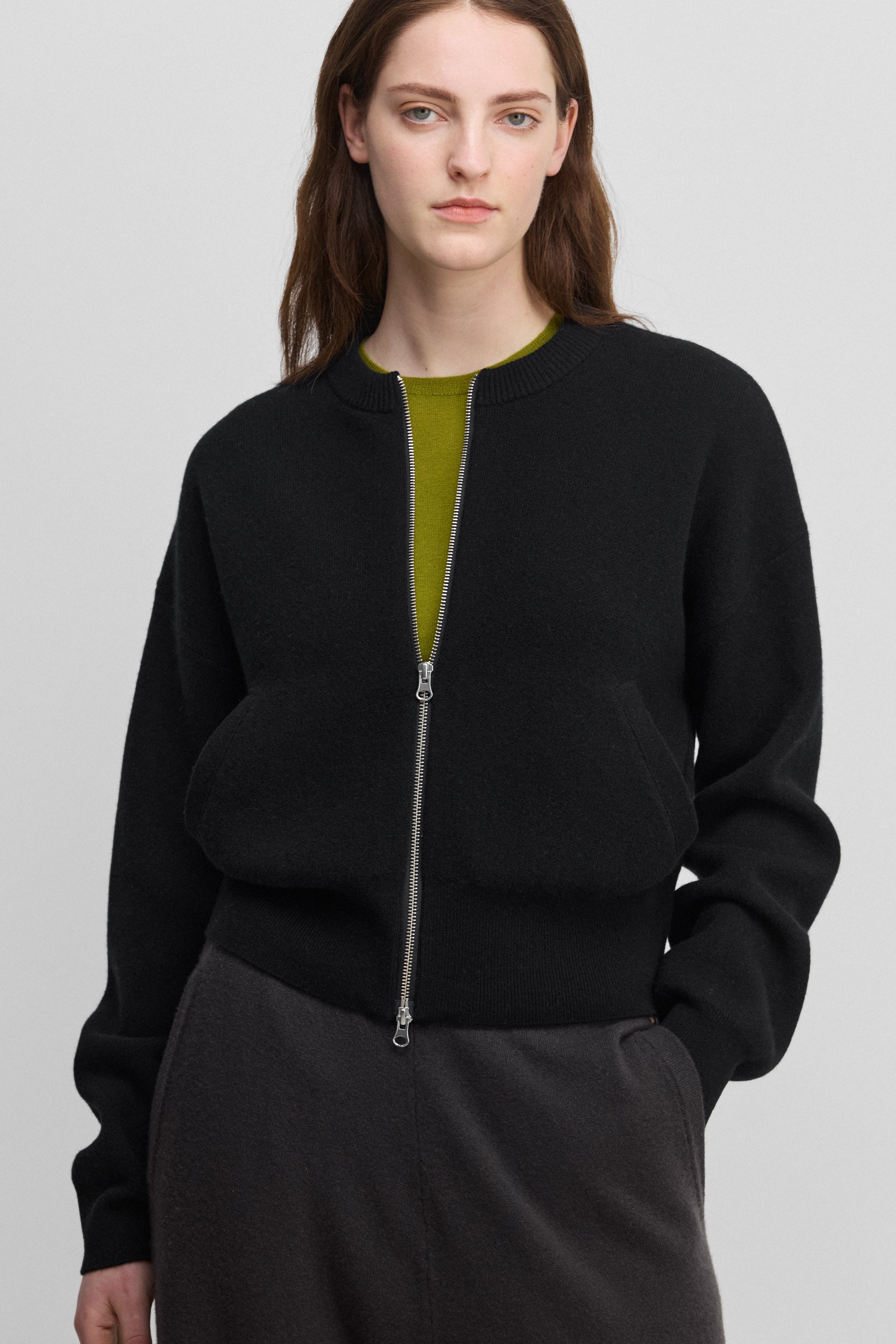 woman wearing a black cashmere crew-neck cardigan with a metallic zipper and side pockets.