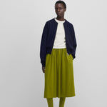 woman wearing a dark blue cashmere crew-neck cardigan with a two-way zipper and side pockets, styled with a green skirt.