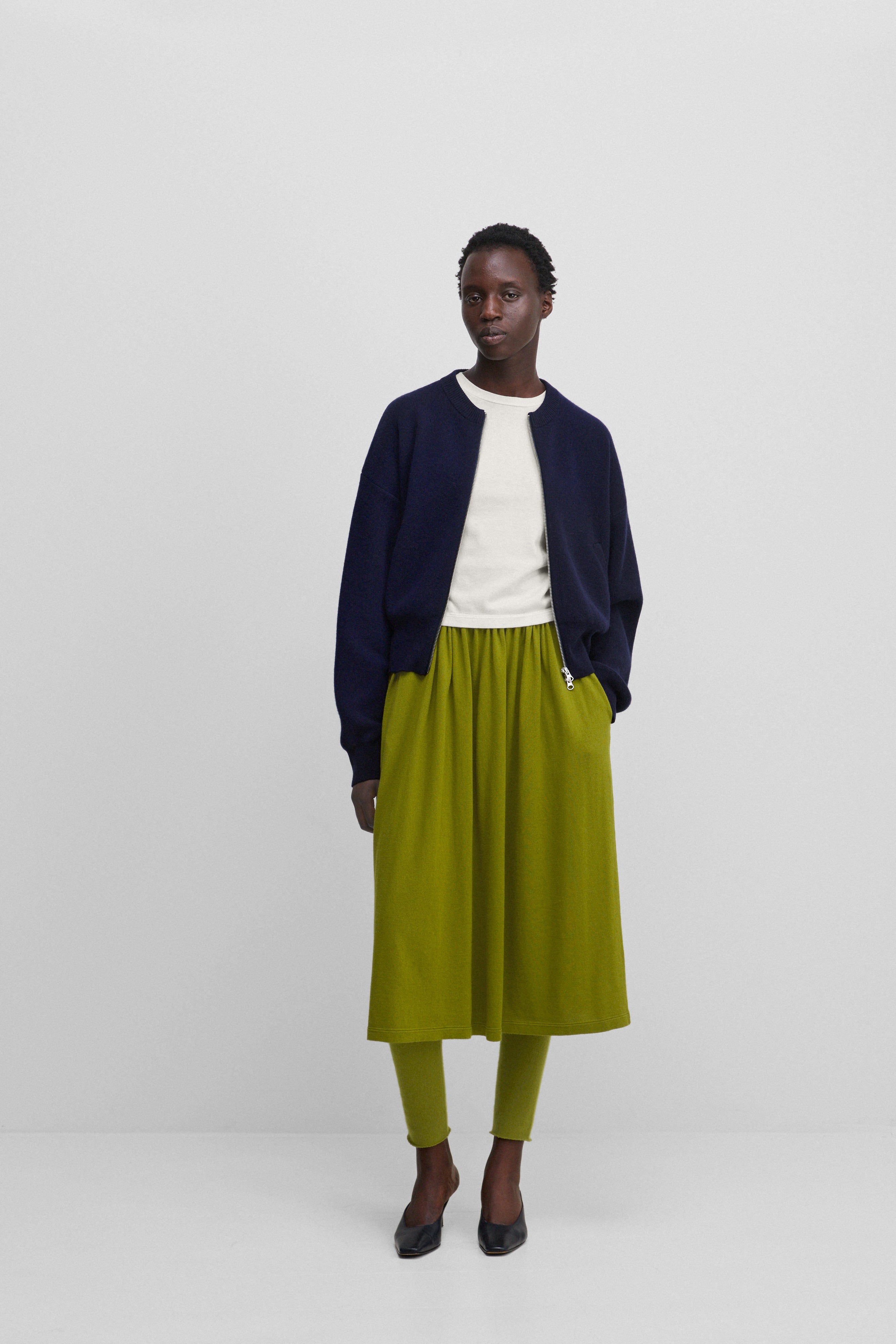 woman wearing a dark blue cashmere crew-neck cardigan with a two-way zipper and side pockets, styled with a green skirt.