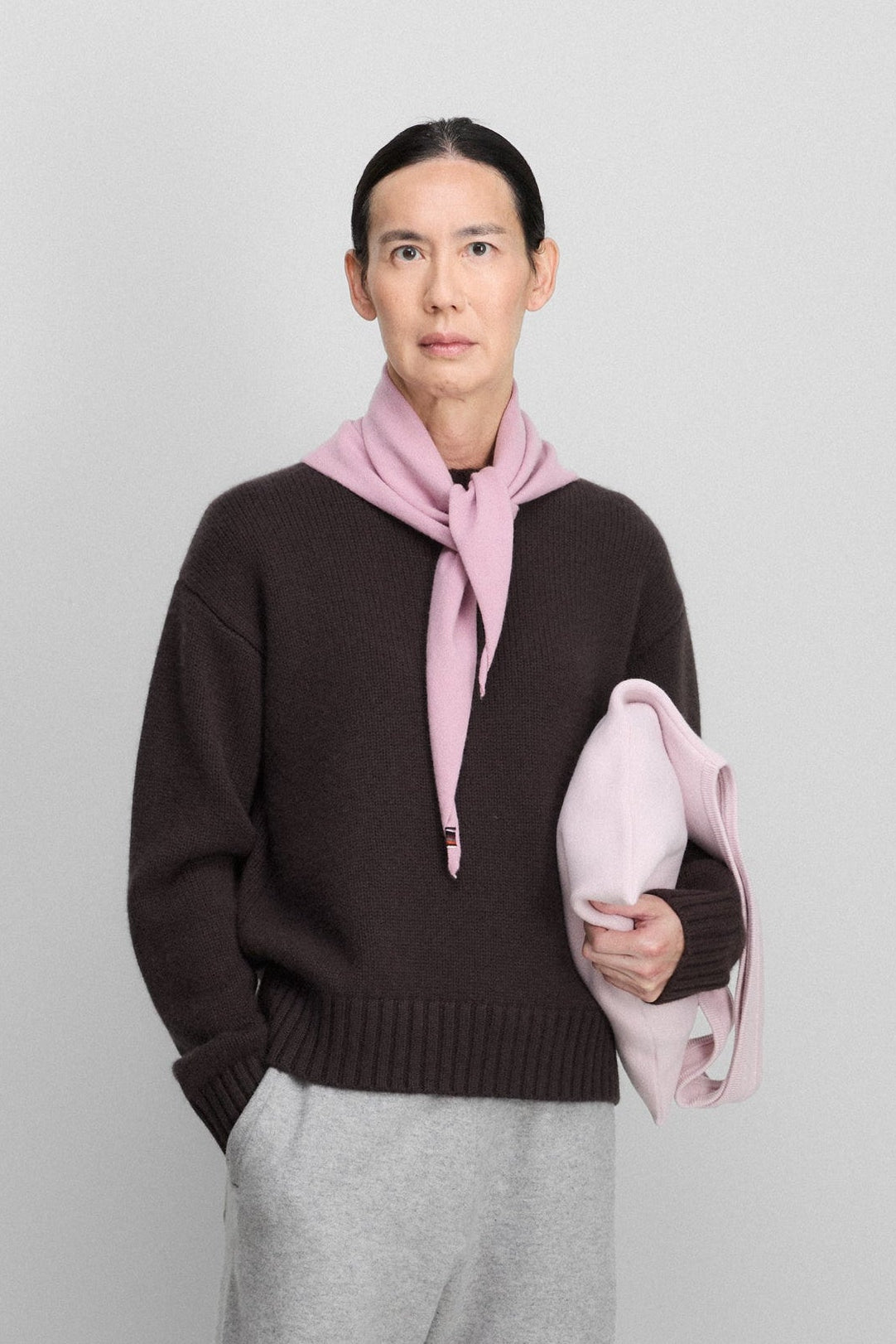 woman wearing a dark brown cashmere crew-neck sweater, styled with a pink scarf.