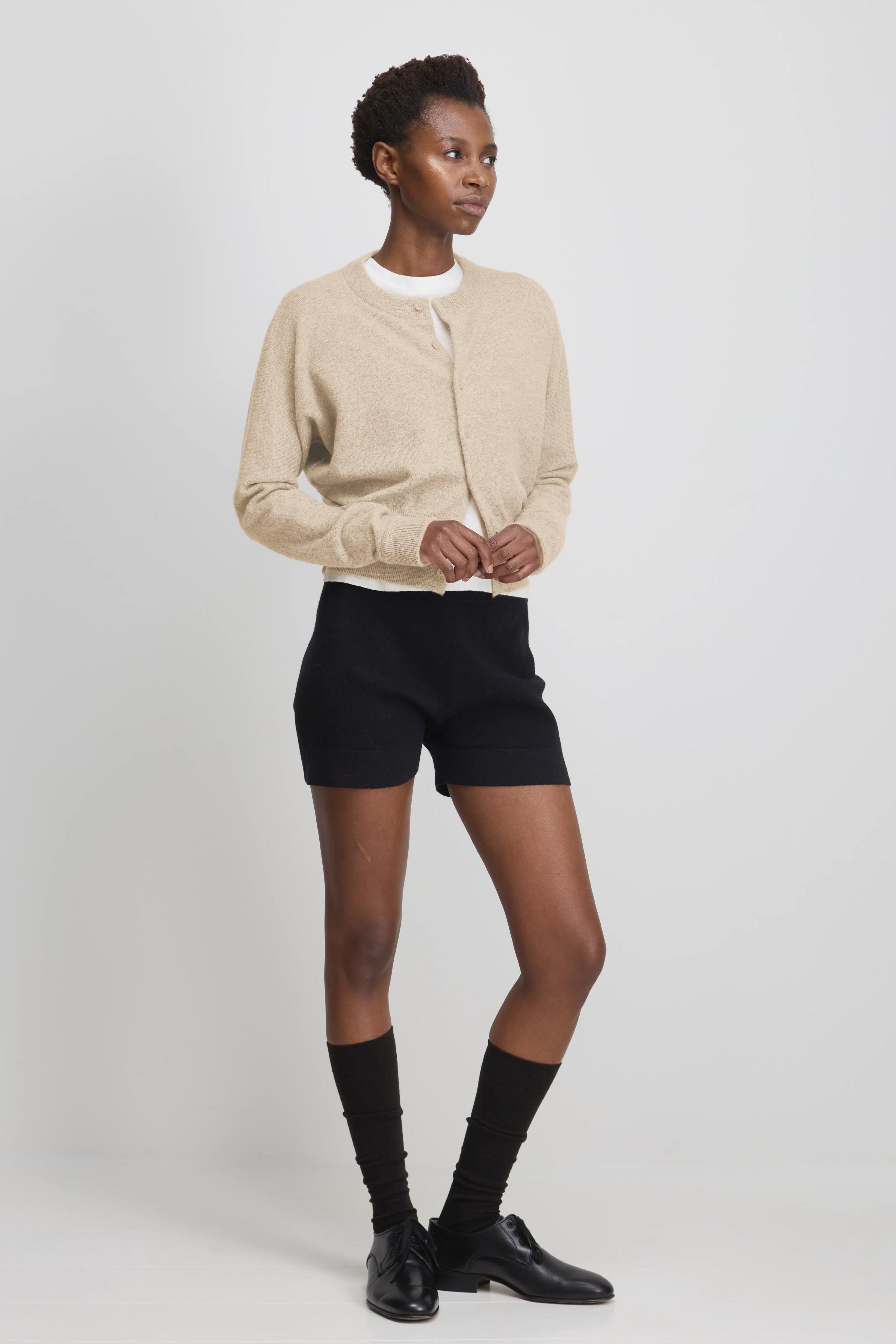woman wearing fitted black cotton cashmere rib-knit shorts, styled with a beige cardigan.