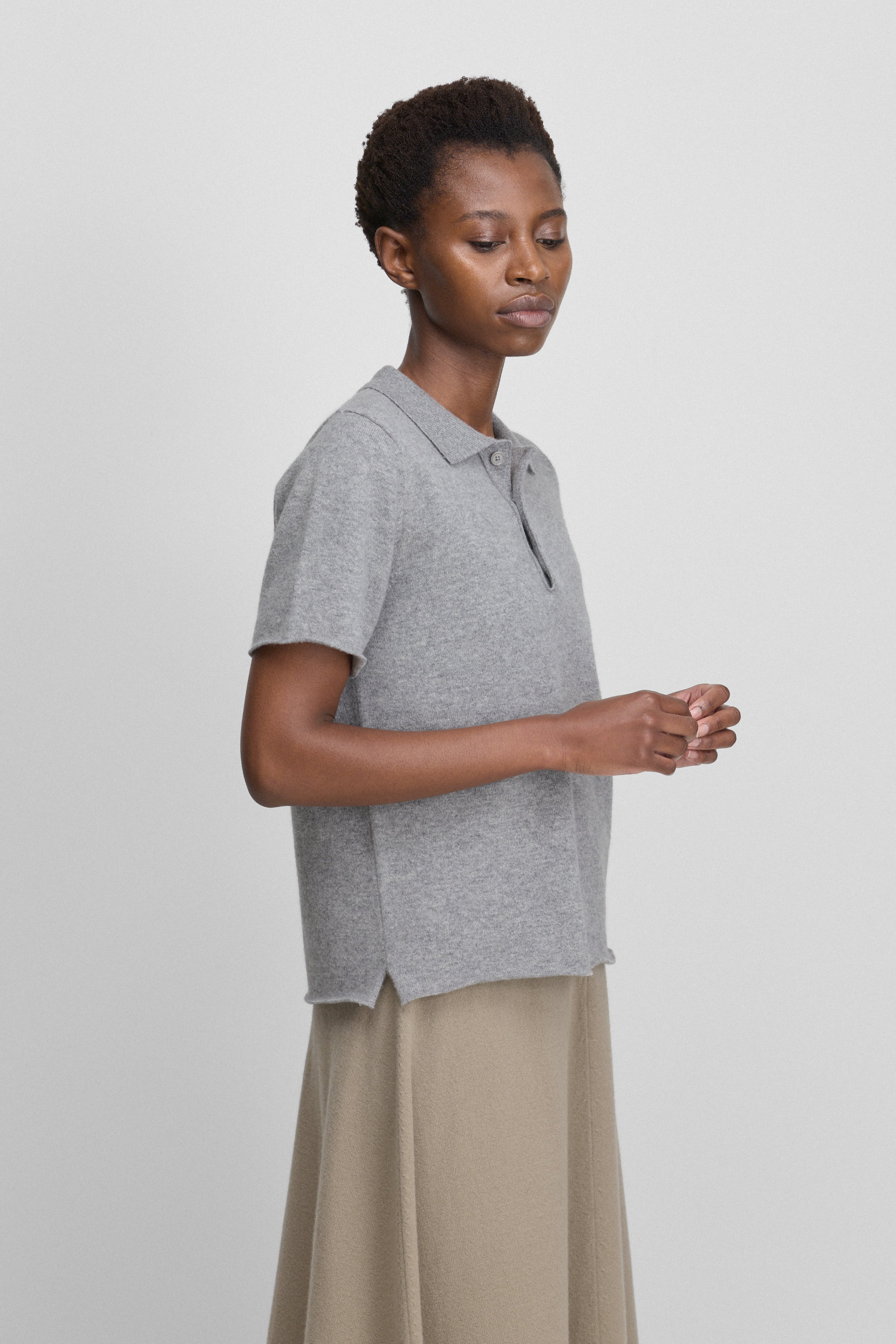 woman wearing a grey short-sleeved cashmere polo shirt with a side split in the bottom hem, shown from the side.