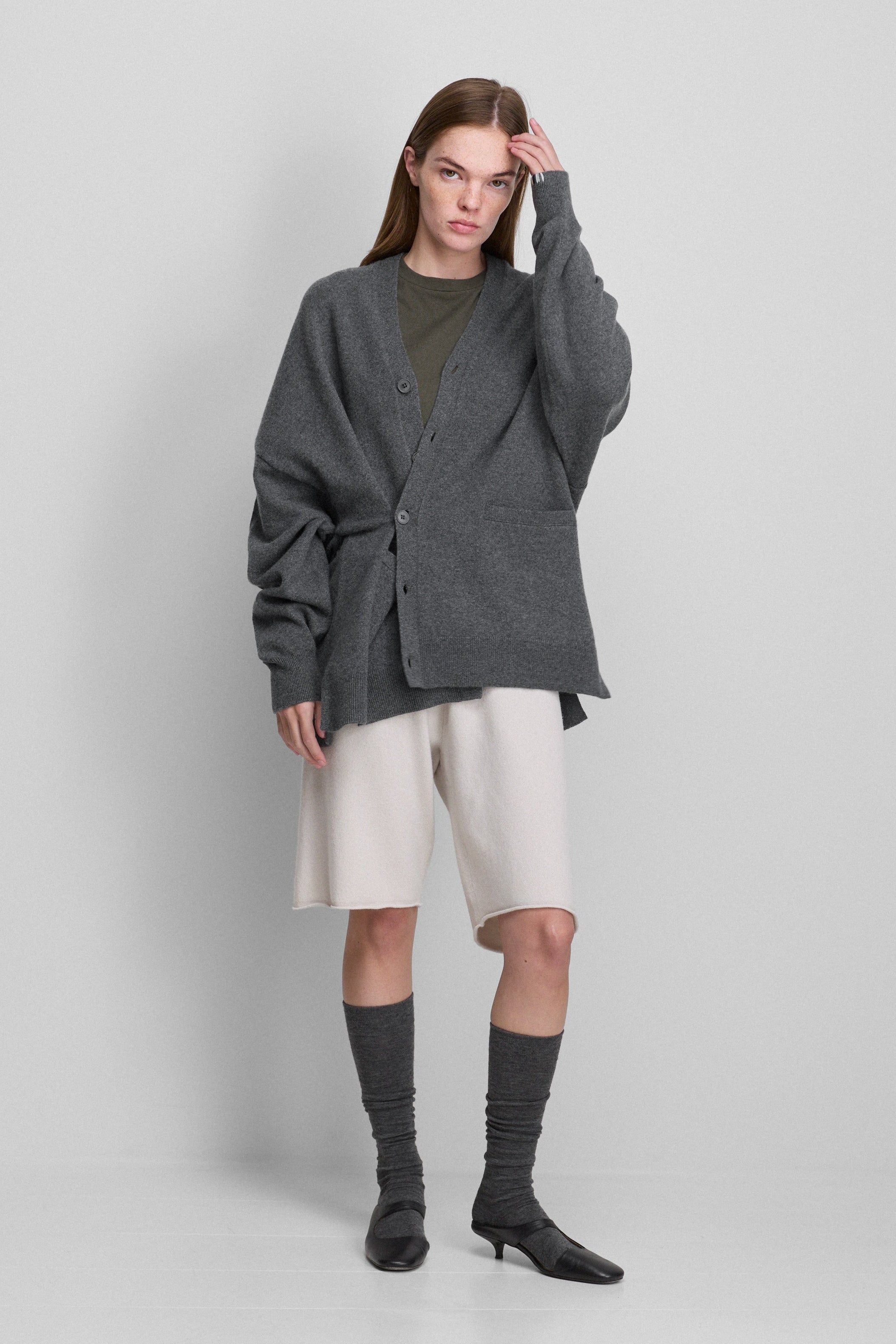 woman wearing an oversized dark grey cashmere v-neck cardigan with five corozo buttons and two front pockets.