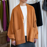 woman wearing an oversized orange cashmere v-neck cardigan with five corozo buttons and two front pockets.