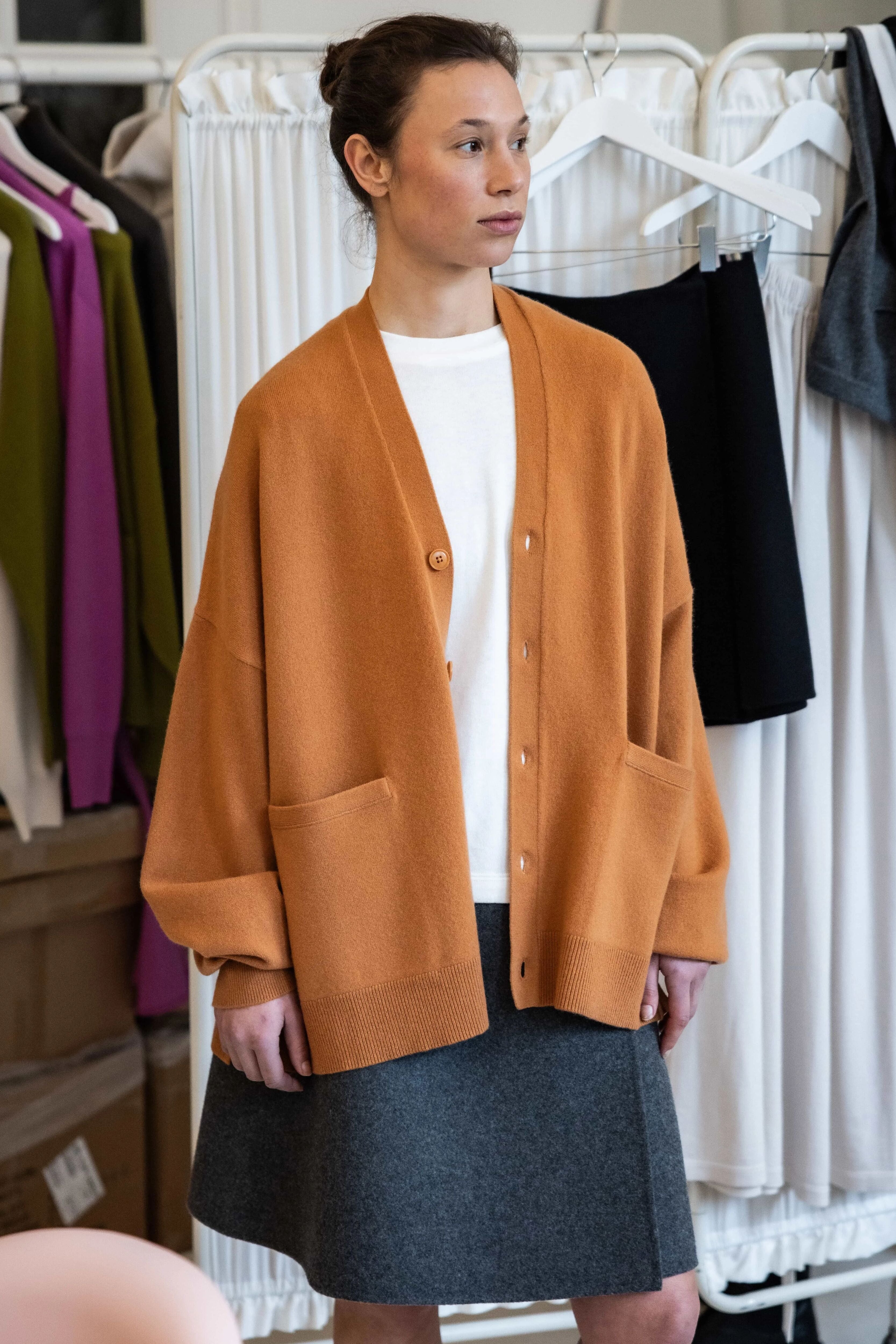 woman wearing an oversized orange cashmere v-neck cardigan with five corozo buttons and two front pockets.