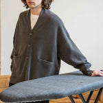 man wearing an oversized dark grey cashmere v-neck cardigan with five corozo buttons and two front pockets.