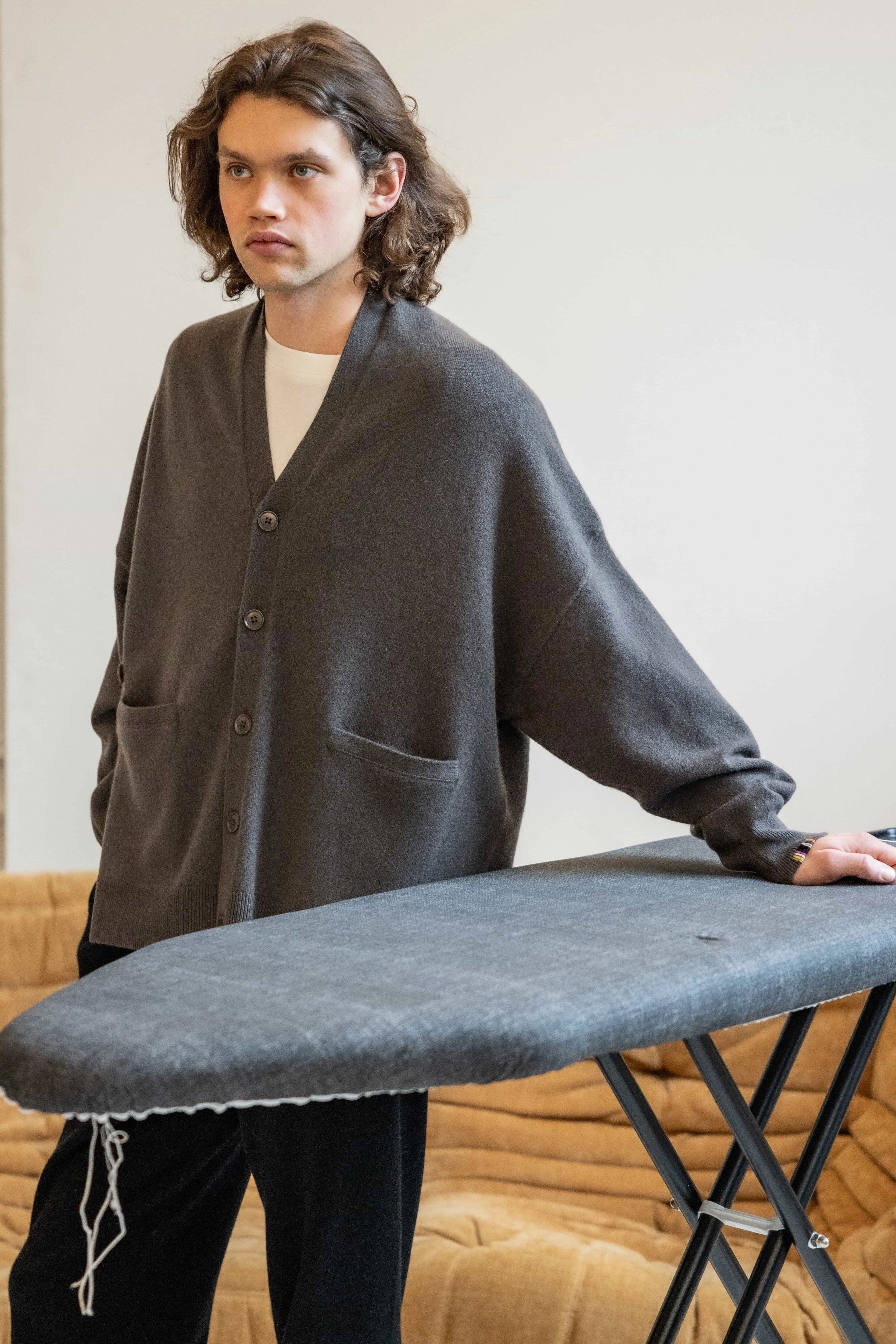 man wearing an oversized dark grey cashmere v-neck cardigan with five corozo buttons and two front pockets.