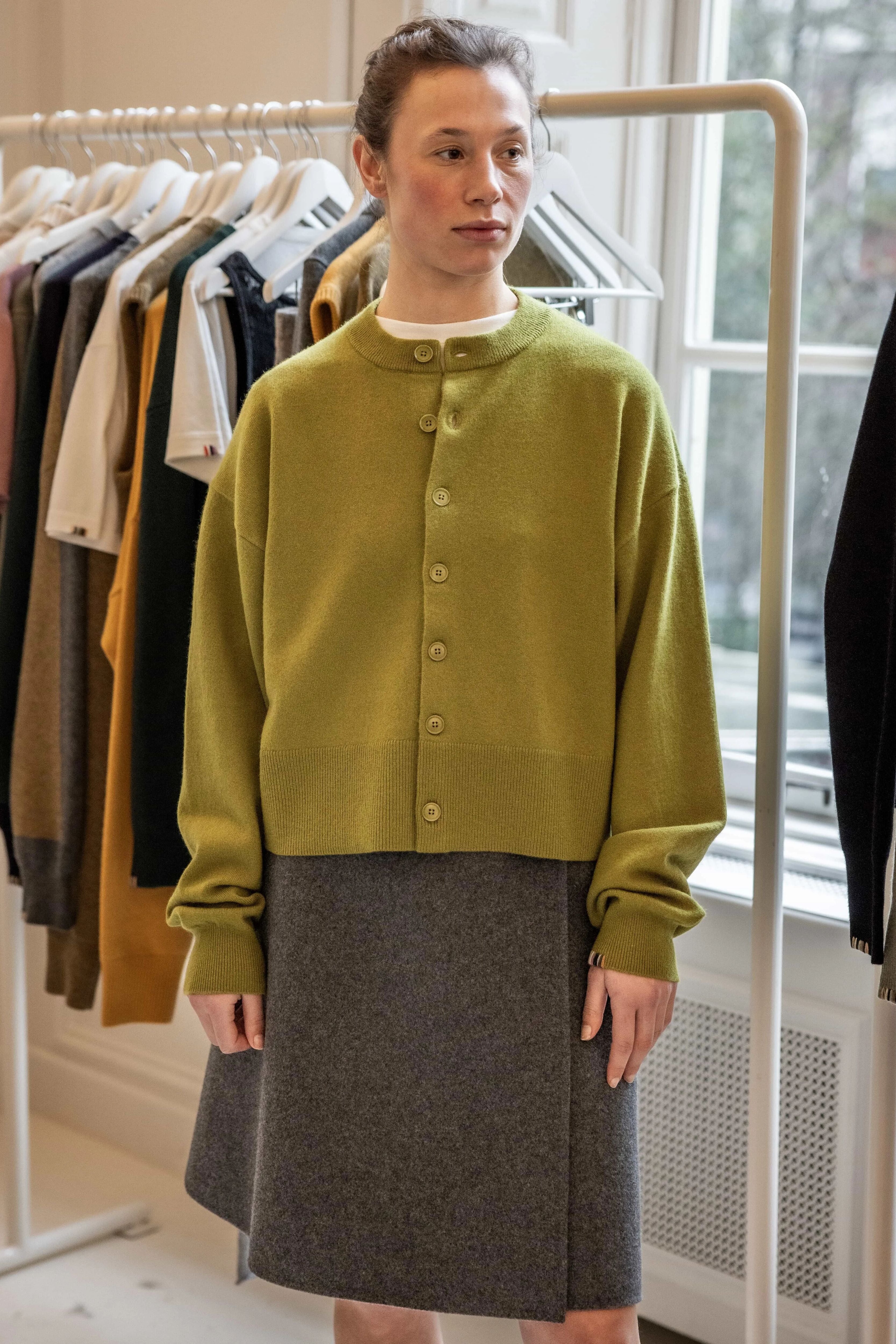 woman wearing a green boxy cashmere crewneck cardigan with seven corozo buttons and ribbed trims.