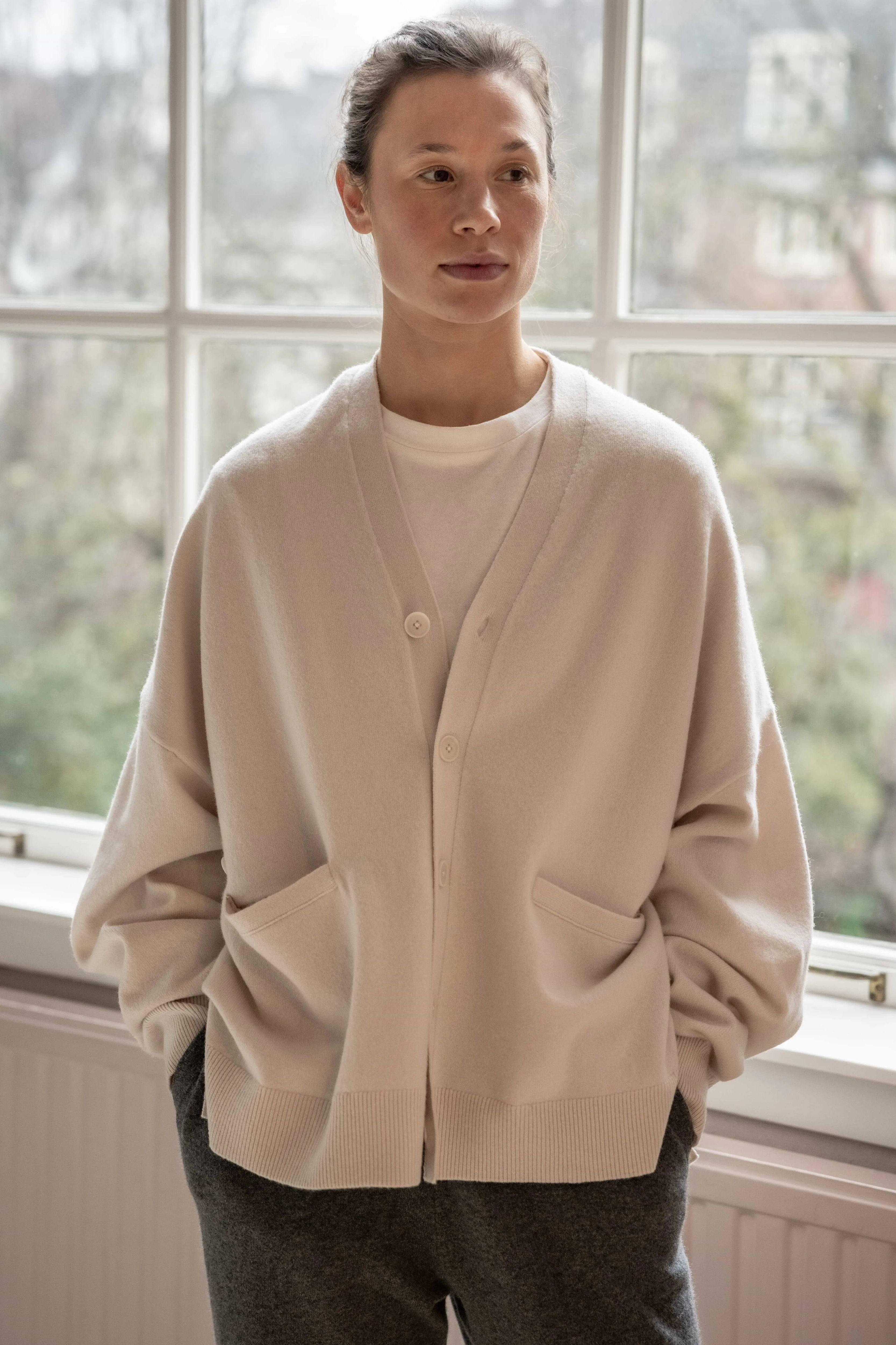 woman wearing an oversized white cashmere v-neck cardigan with five corozo buttons and two front pockets.