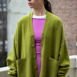 woman wearing an oversized green cashmere v-neck cardigan with five corozo buttons and two front pockets.
