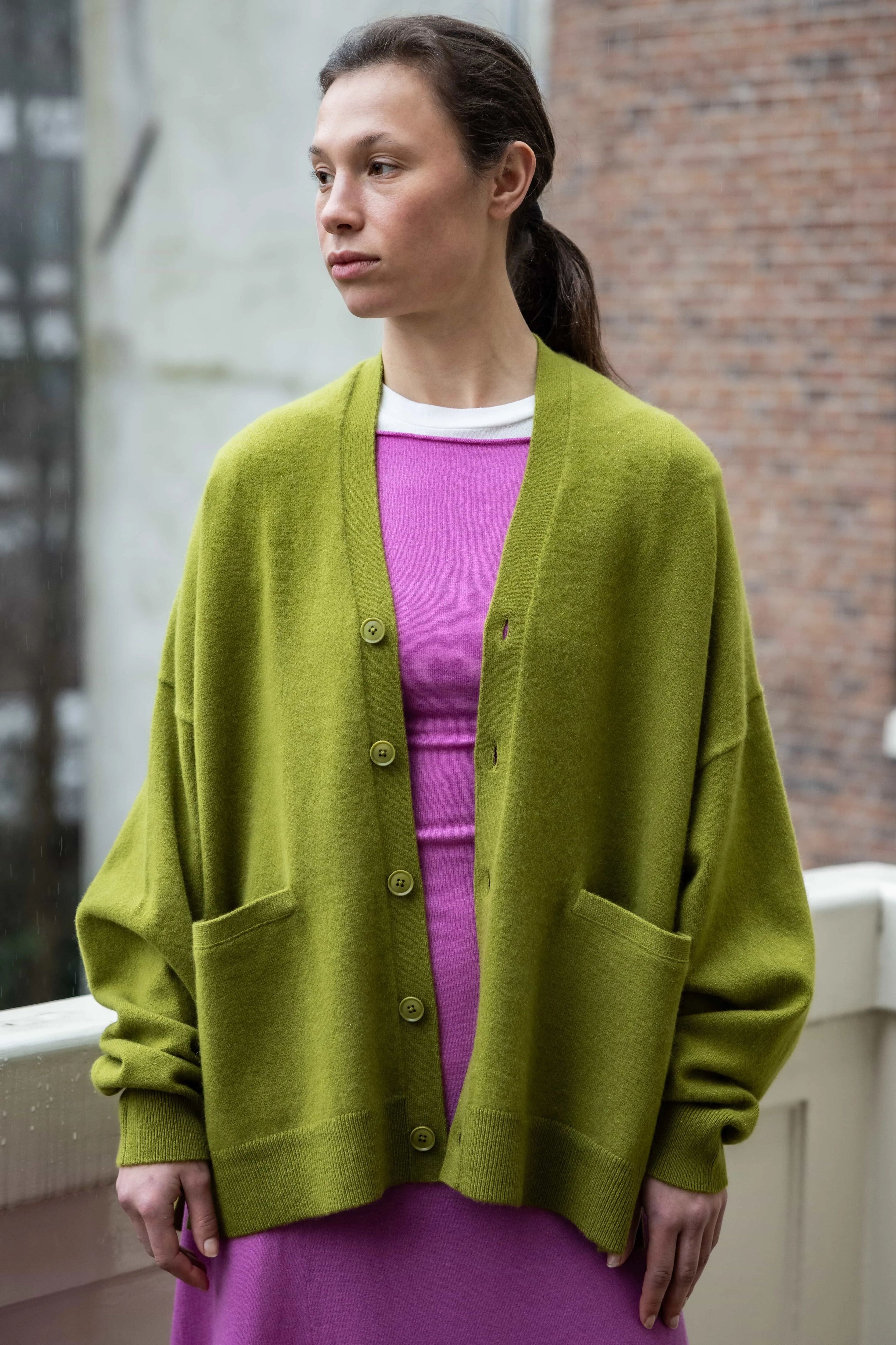 woman wearing an oversized green cashmere v-neck cardigan with five corozo buttons and two front pockets.