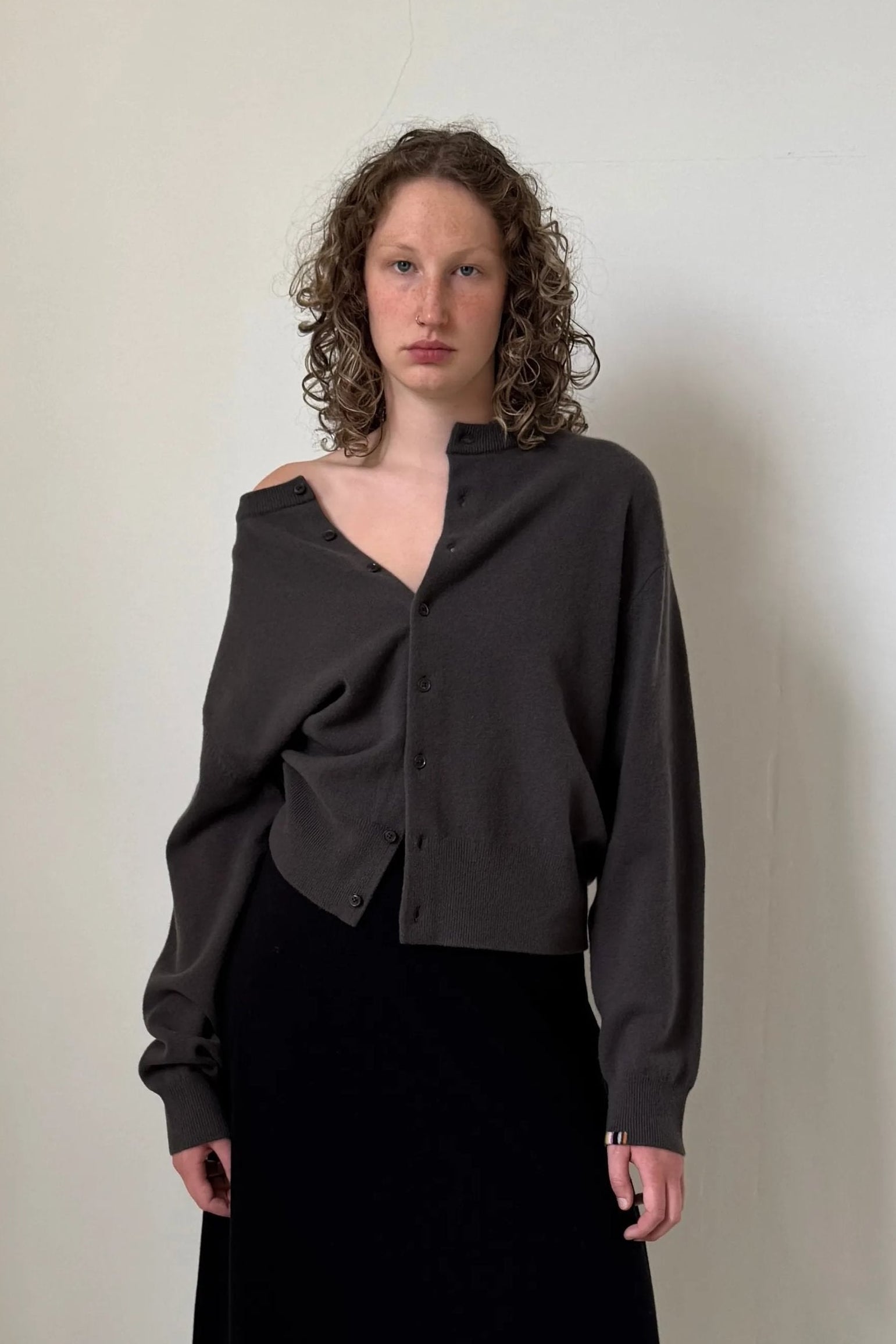woman wearing a dark grey boxy cashmere crewneck cardigan with seven corozo buttons and ribbed trims.